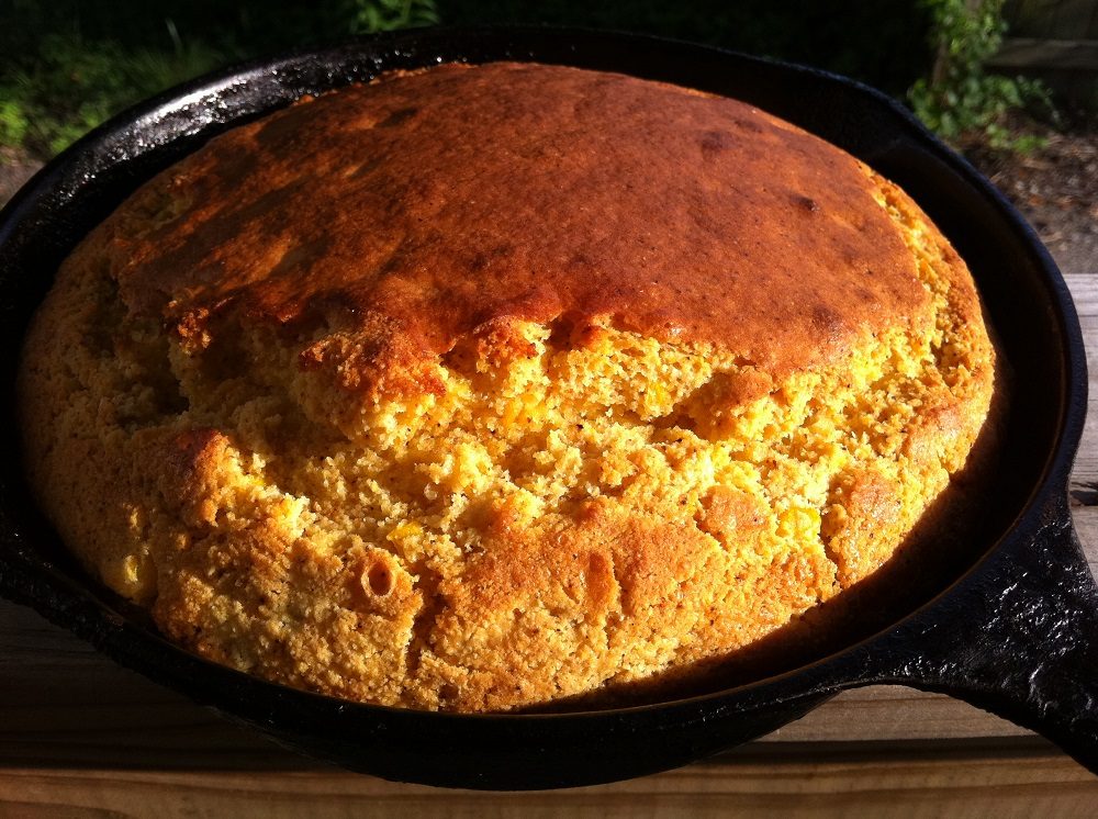 Freshly baked cornbread with golden crust in a cast iron skillet on wooden surface.