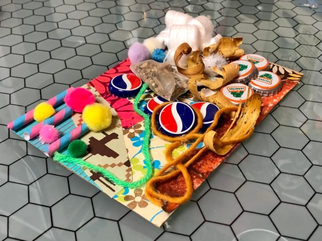 Assorted craft materials on hexagonal-pattern surface with pom-poms, caps, ribbon, and beads.