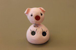 Small pig figurine with button eyes, red nose, soft material, on neutral background.