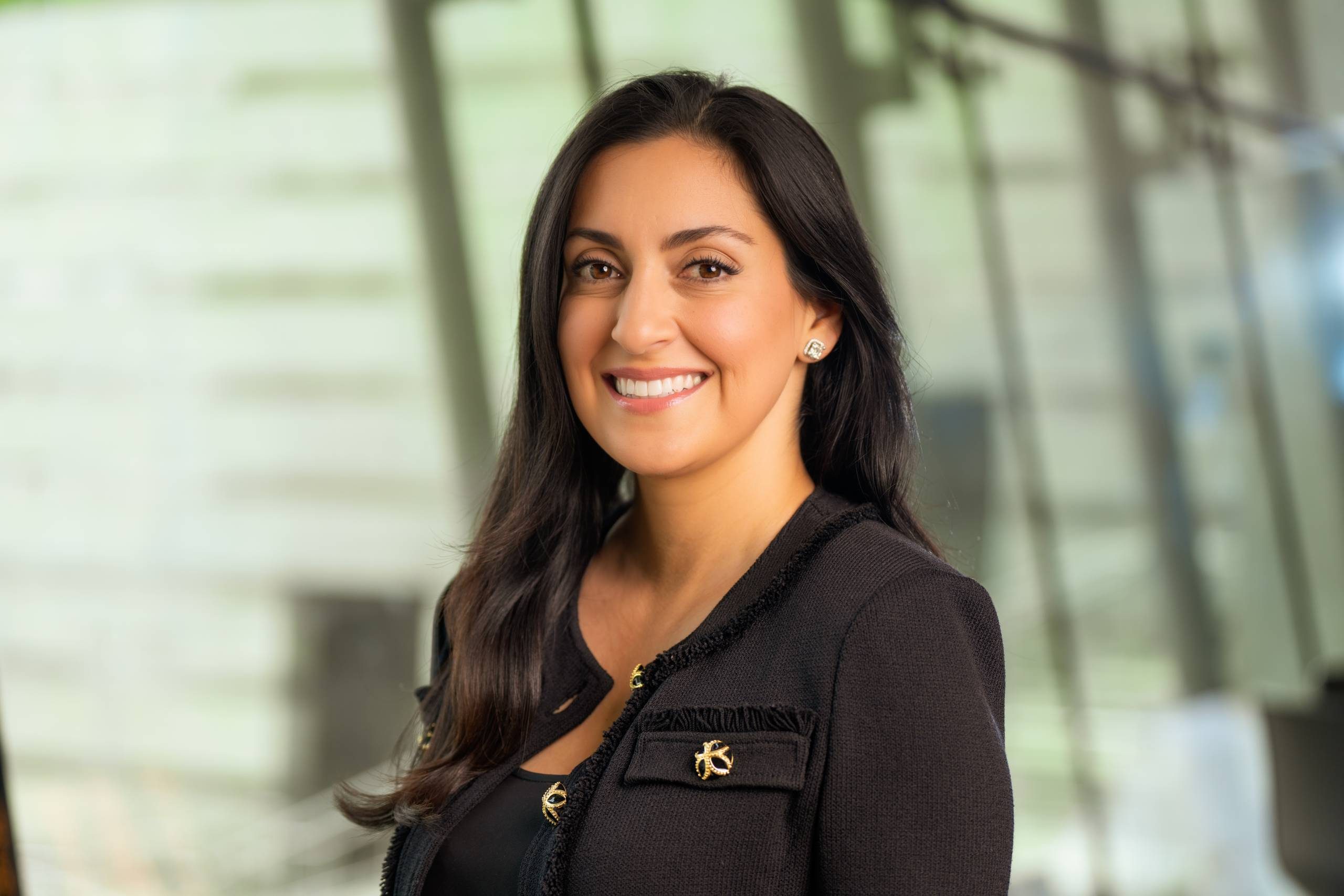 A woman with dark hair smiling in Eleven at Crystal Bridges in a black jacket with gold buttons