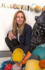 Person with long hair in dark blazer crouching among colorful buoys and maritime objects.