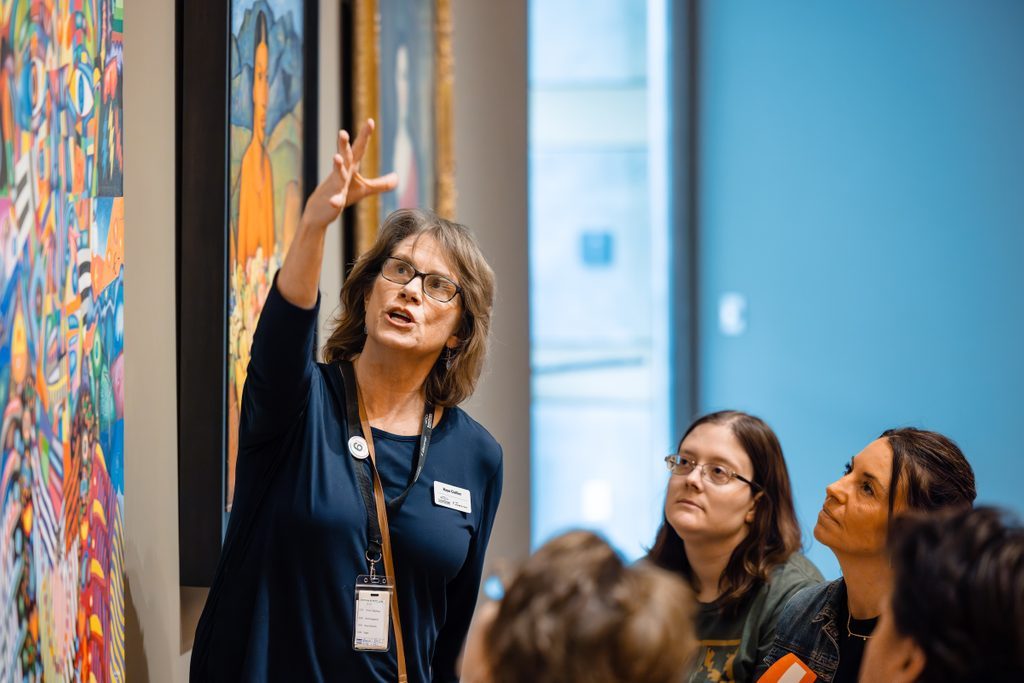Woman discussing colorful painting with attentive gallery group.