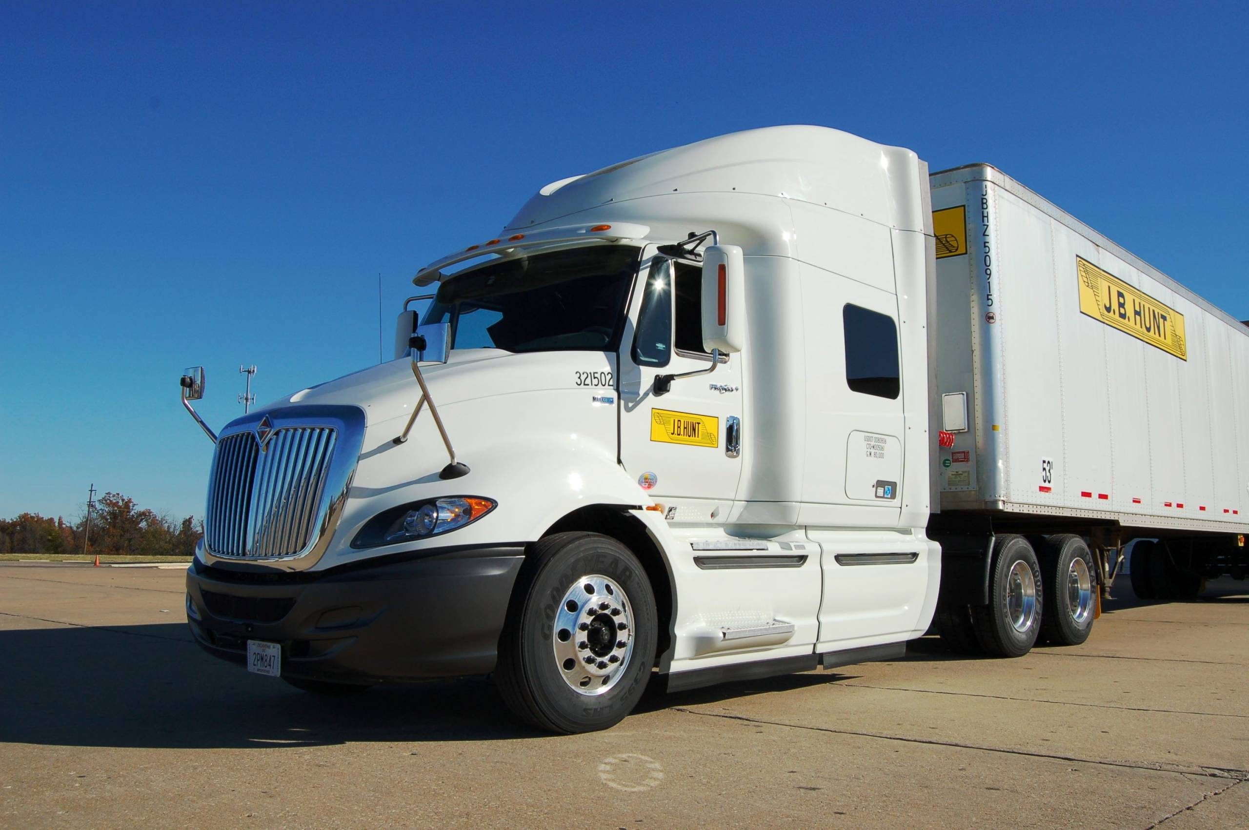 White semi-truck with J.B. Hunt trailer parked, clear sky, trees in background.