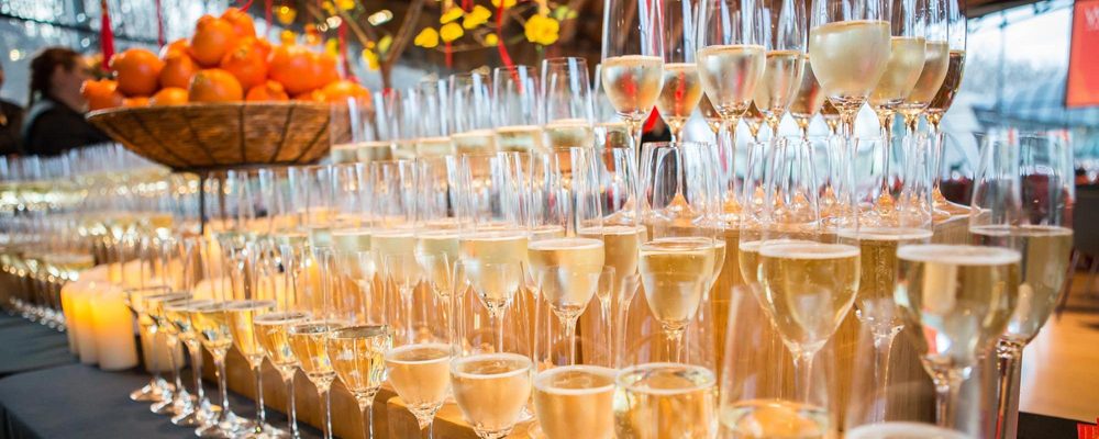 Rows of wine glasses on a wooden display stand, sitting on a black table cloth next to a floral arrangement