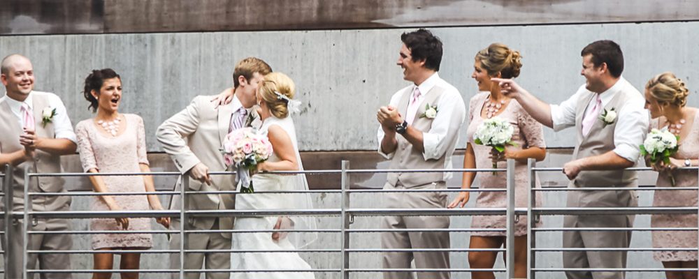 Wedding party in formal attire on metal railing with pink ties and dresses, holding bouquets.