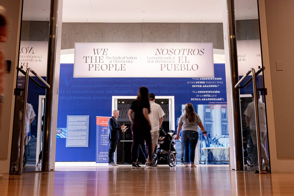 a group of people walk toward an exhibition door under a banner that says 