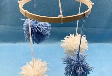 blue and white pom poms hanging from a circular wooden frame against a blue backdrop