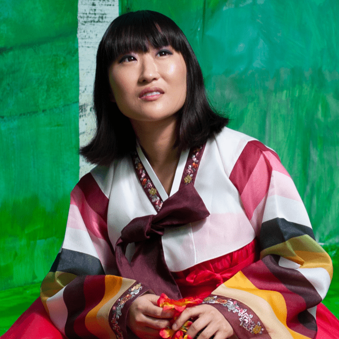 Person in vibrant Korean hanbok with striped sleeves, green background.